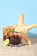Glasses of cold Cuba Libre cocktail and starfish on sand near blue background