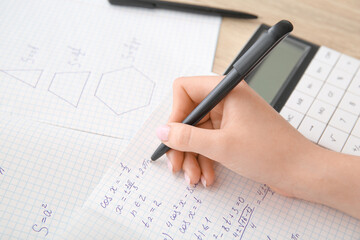 Woman writing math formulas in copybook on wooden table