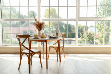 Autumn table setting with pampas grass and pumpkins in light kitchen near big window