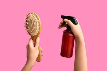 Female hands with hairbrush and sprayer on pink background.