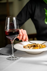 A close-up view of a hand holding a fork, savoring a delicious meal with a glass of red wine on a table. The ambiance is elegant, showcasing fine dining settings.