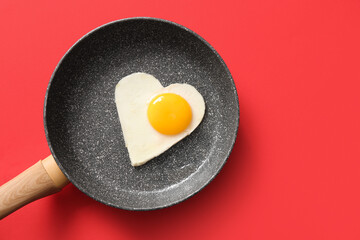 Frying pan with tasty fried egg in shape of heart on red background