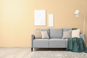 Stylish grey sofa with pillows, blanket and paintings near beige wall