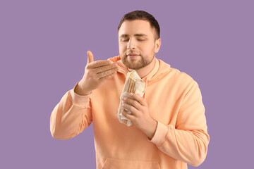 Handsome young man with tasty doner kebab on lilac background
