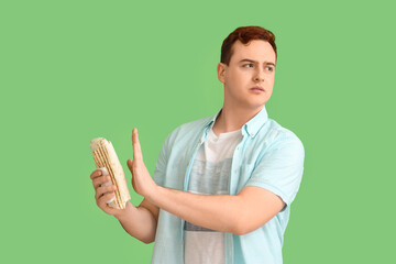 Young man refusing to eat doner kebab on green background