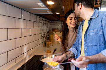 Couple enjoying a joyful moment while cooking pasta together in a modern kitchen, with the man...