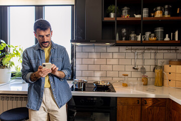 Man preparing food in a modern kitchen while using a smartphone, blending technology and culinary skills in a stylish home environment