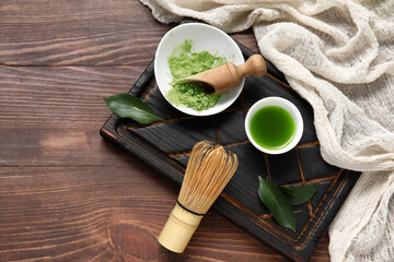 Bowls of matcha tea and powder with chasen on wooden background