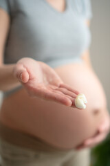 Pregnant woman gently applies moisturizing cream to her belly, focusing on skincare and reducing stretch marks during pregnancy. Focus on hand with cream