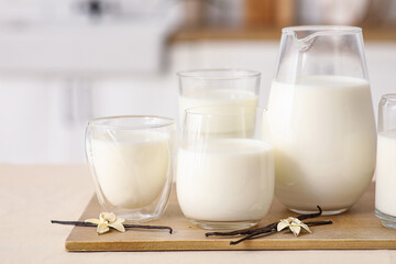 Glasses and jug of fresh vanilla milk with sticks and flowers on table in kitchen