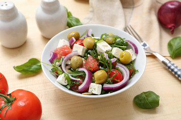 Bowl of healthy vegetable salad with feta cheese, onion, arugula, olives and grapefruit on wooden background