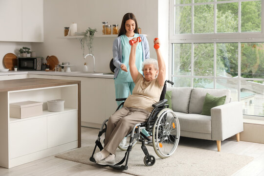 Young caregiver and senior woman in wheelchair with dumbbells training at home