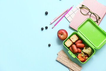 Lunch box with tasty food and school stationery on blue background