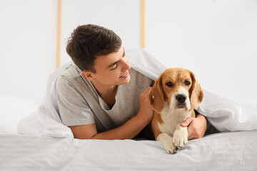 Young man in bed hugging adorable Beagle dog at home