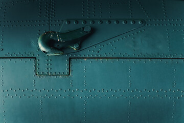 Aluminum surface of a vintage aircraft fuselage with a hook attached to the body of the plane