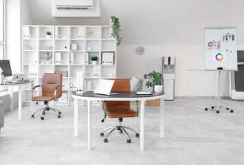 Interior of light open space office with workplaces, shelving unit and armchairs