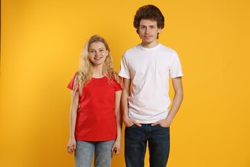 Young woman and man wearing blank t-shirts on orange background. Mockup for design