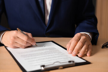 Man putting signature on document at wooden table, closeup