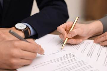 Woman pointing at document and man putting signature at table, closeup