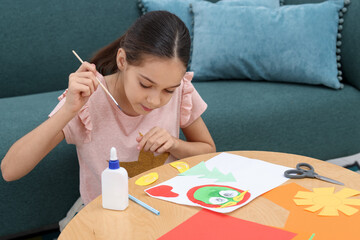 Girl applying glue onto paper figure for her creative project at table indoors. Art and craft