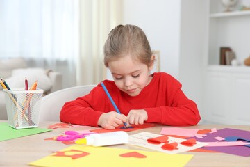 Little girl making handmade project with color paper and pencil at table indoors