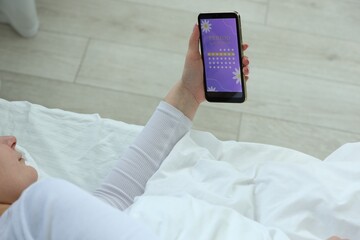 Menstruation. Woman using period calendar application on smartphone in bed indoors, above view