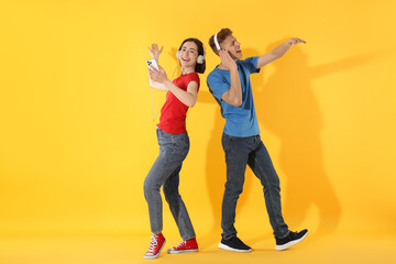 Fototapeta premium Happy couple in headphones dancing on yellow background. Space for text