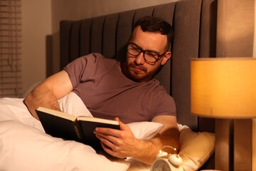 Young man reading book in bed at home