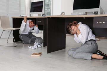 Scared employees hiding under office desks during earthquake