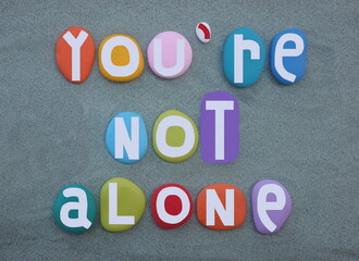 You are not alone, creative social slogan composed with multi colored hand painted stone letters over green sand