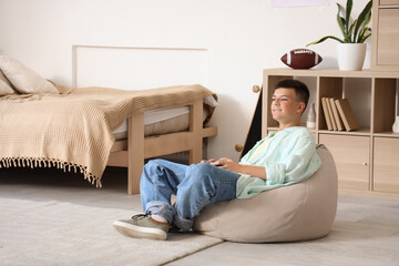 Teenage boy playing video game on beanbag in bedroom