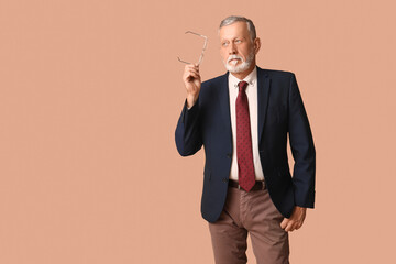 Handsome thoughtful mature man in stylish formal suit with tie on beige background