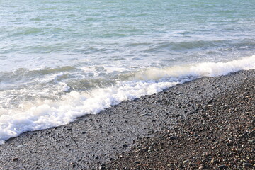 Beautiful pebble beach with calm sea waves and blue sky. Natural seaside landscape with soft sunlight, peaceful atmosphere, and clear water. Summer vacation concept.