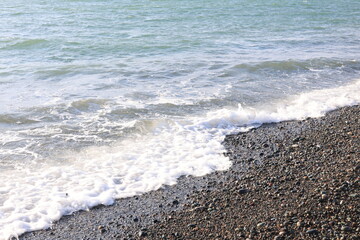Beautiful pebble beach with calm sea waves and blue sky. Natural seaside landscape with soft sunlight, peaceful atmosphere, and clear water. Summer vacation concept.