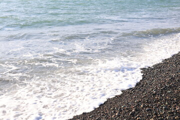 Beautiful pebble beach with calm sea waves and blue sky. Natural seaside landscape with soft sunlight, peaceful atmosphere, and clear water. Summer vacation concept.