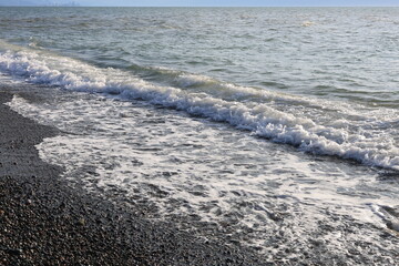 Beautiful pebble beach with calm sea waves and blue sky. Natural seaside landscape with soft sunlight, peaceful atmosphere, and clear water. Summer vacation concept.