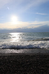 Beautiful pebble beach with calm sea waves and blue sky. Natural seaside landscape with soft sunlight, peaceful atmosphere, and clear water. Summer vacation concept.