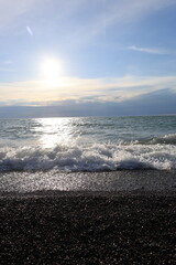 Beautiful pebble beach with calm sea waves and blue sky. Natural seaside landscape with soft sunlight, peaceful atmosphere, and clear water. Summer vacation concept.
