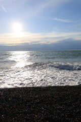 Beautiful pebble beach with calm sea waves and blue sky. Natural seaside landscape with soft sunlight, peaceful atmosphere, and clear water. Summer vacation concept.