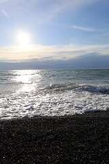 Beautiful pebble beach with calm sea waves and blue sky. Natural seaside landscape with soft sunlight, peaceful atmosphere, and clear water. Summer vacation concept.