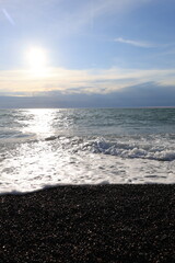 Beautiful pebble beach with calm sea waves and blue sky. Natural seaside landscape with soft sunlight, peaceful atmosphere, and clear water. Summer vacation concept.