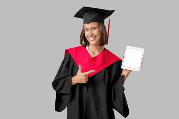Female graduating student with tablet computer on grey background