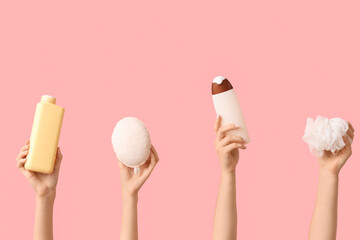 Female hands with bottles of cosmetic products and bath sponges on pink background