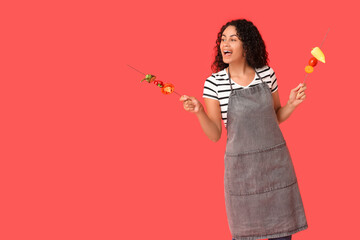Beautiful young happy African-American woman with tasty vegetables skewers on red background