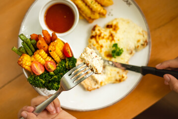 Close up sliced chicken steak with melted cheese. Cut with knife and fork. Served with bbq sauce, vegetables and fries. Perfectly for advertising and commercial purpose