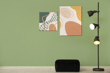Floor lamp, pouf and pictures near green wall in room