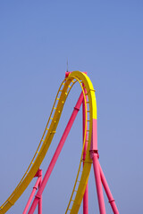 colorful roller coaster track features bright yellow and pink design against clear blue sky,...