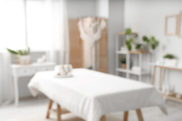 Blurred view of light spa salon with massage couch, shelf units and tables