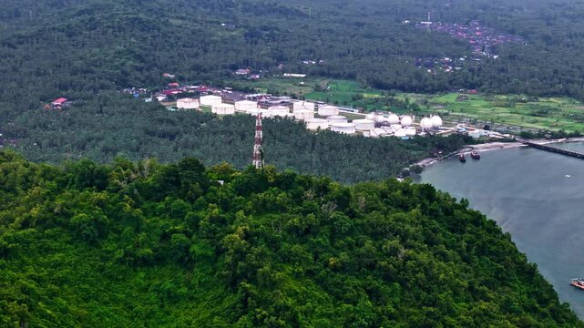 Industrial Pertamina oil terminal in Manggis, Bali seen from above with ocean backdrop, aerial pullback overview
