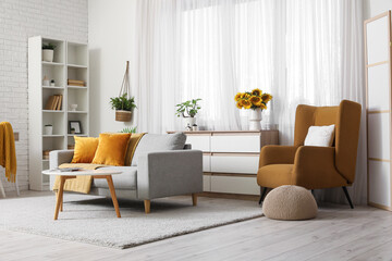 Interior of living room with sunflowers on chest of drawers, armchair and cozy sofa